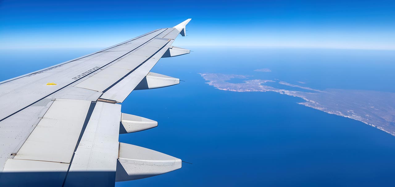 Airplane wing flying over Greek islands and the blue Aegean Sea