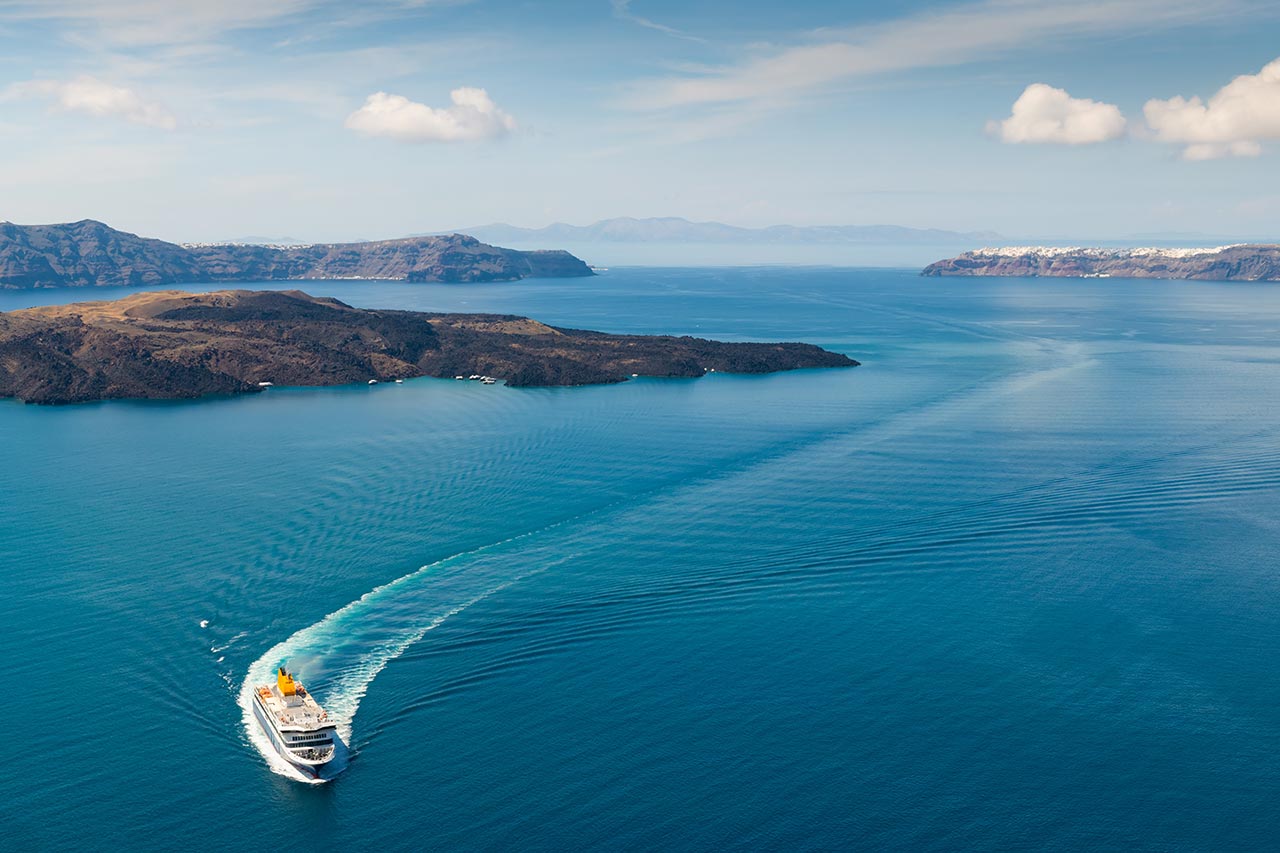 Aerial view of a ferry sailing between Greek islands leaving a curved wake in the sea