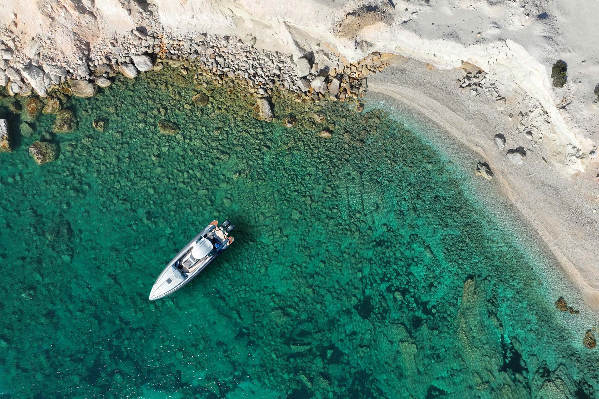 Aerial view of Kastanas Beach in Milos with clear emerald water and anchored boat