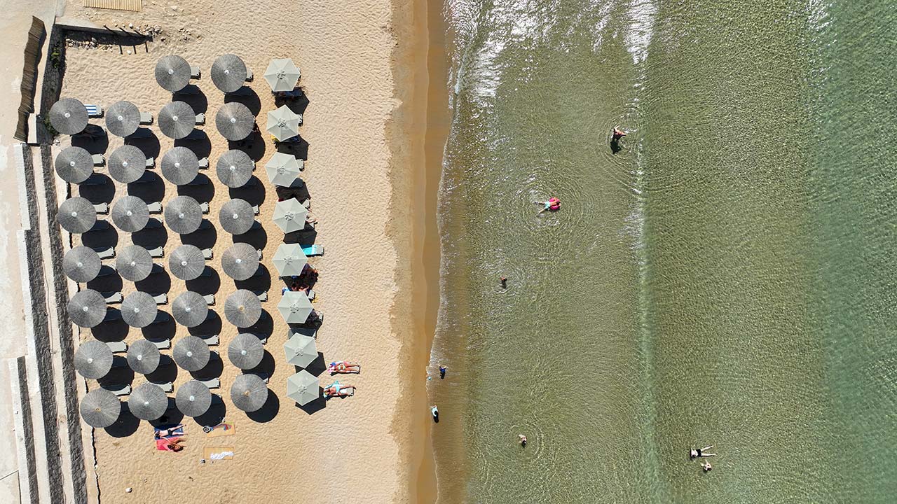 Aerial view of Provatas Beach in Milos with sandy shoreline and swimmers in shallow water