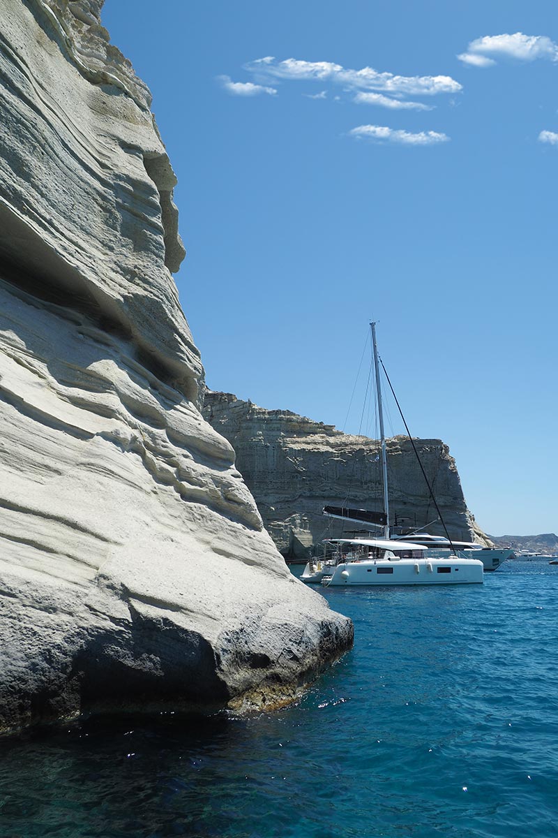 Catamaran sailing near white volcanic cliffs on a Milos boat tour